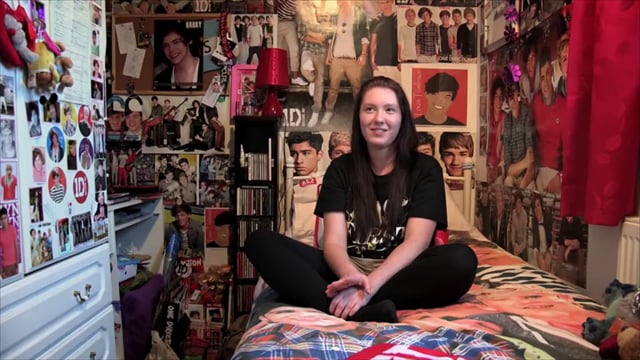 A girl sits on her bed surrounded by posters