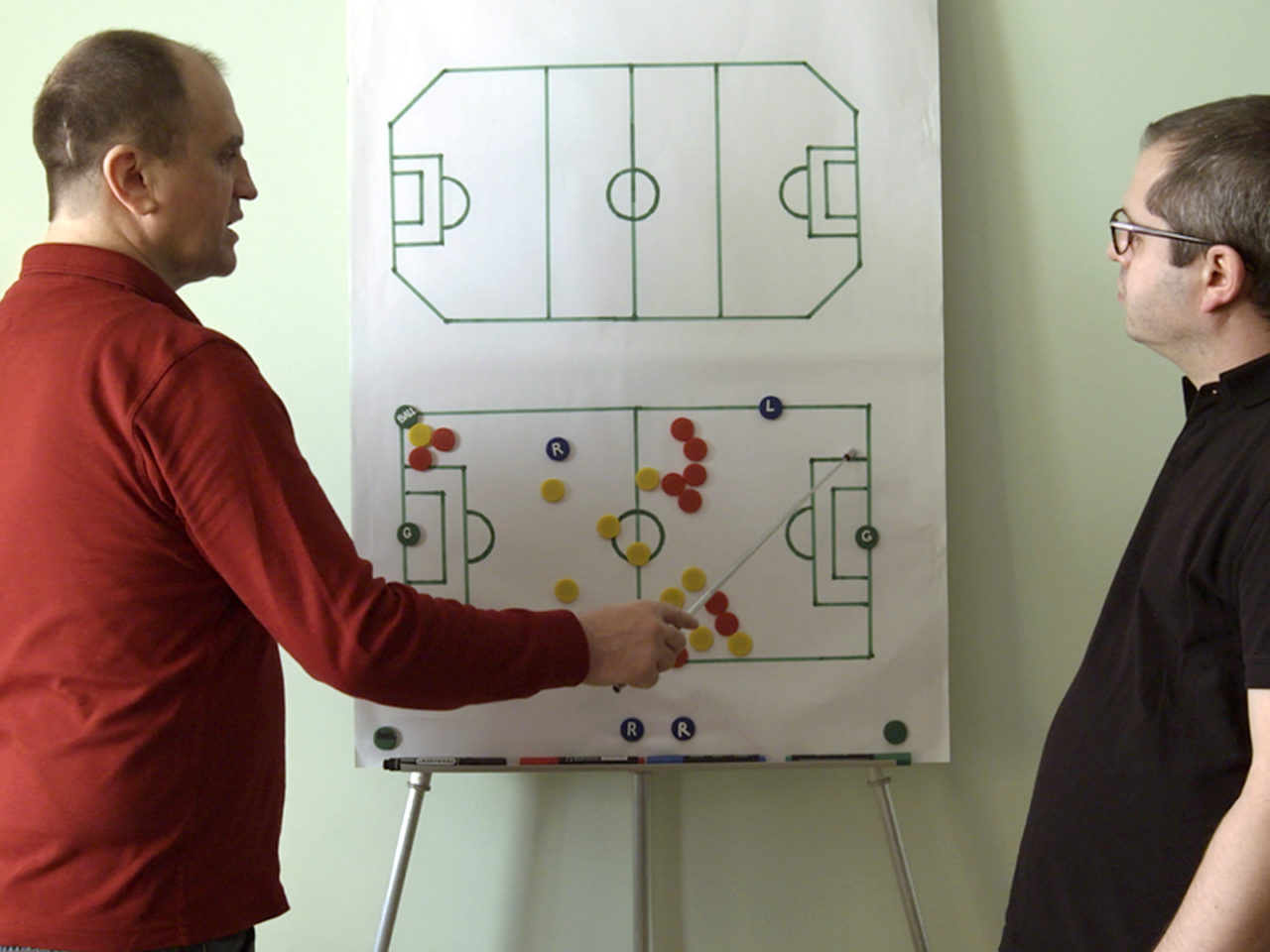 Two men look at a whiteboard with football strategies on