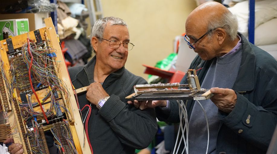 Two old man with grey hair look at each other smiling and working on a pipe organ