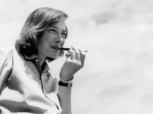Black and White image of author Patricia Highsmith, standing to the left of the image smoking to the backdrop of a cloudy sky.